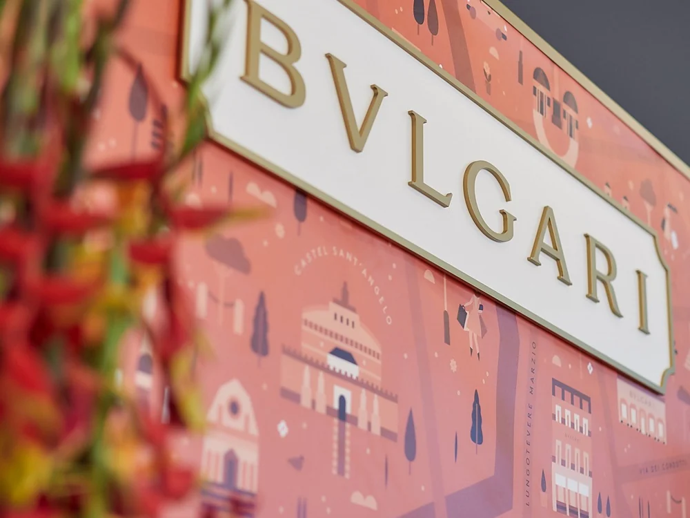 Un photocall illustré de monuments de Rome, avec une plaque en relief et des fleurs rouges au premier plan